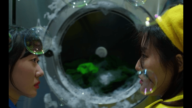 Two women talking in front of a broken washing machine