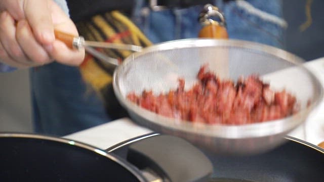 Straining the fried meat through a sieve and putting it in a pot of water