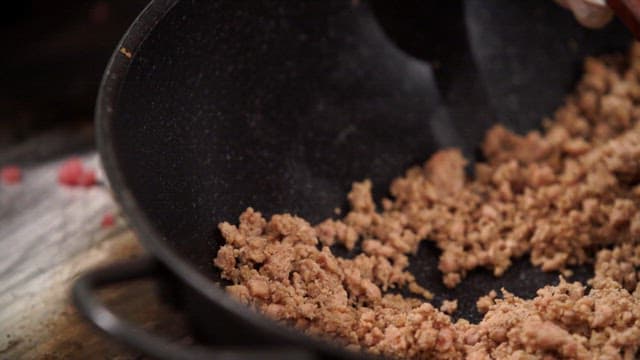 Ground meat being cooked in a pan with a wooden spatula