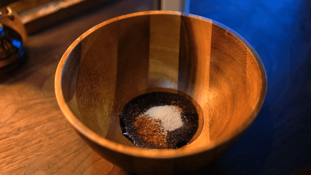 Preparing a wooden bowl with soy sauce, chili flakes, and salt