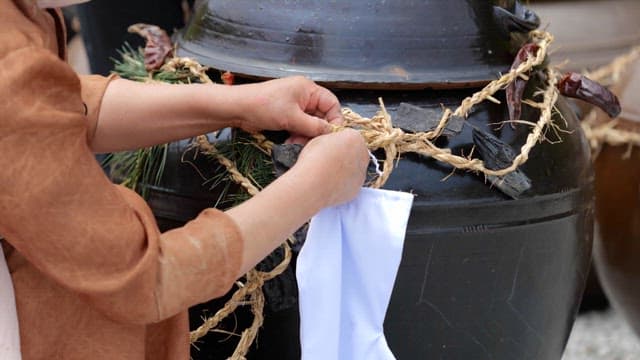 Person Hanging a Beoseon on a Geumjul Wrapped around a Large Crock