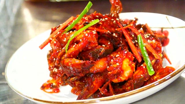 Sprinkling sesame seeds on spicy marinated crab in a bowl