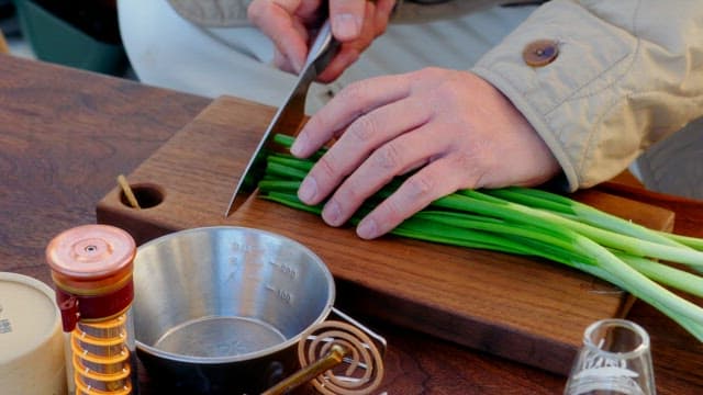 Person chopping green onions on a wooden cutting board