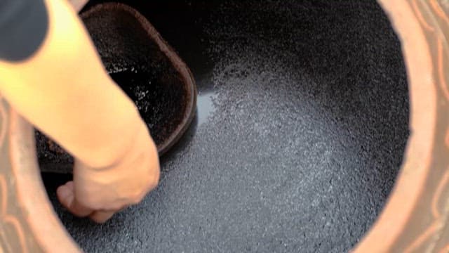 Hand Stirring Dark Soy Sauce in a Earthenware