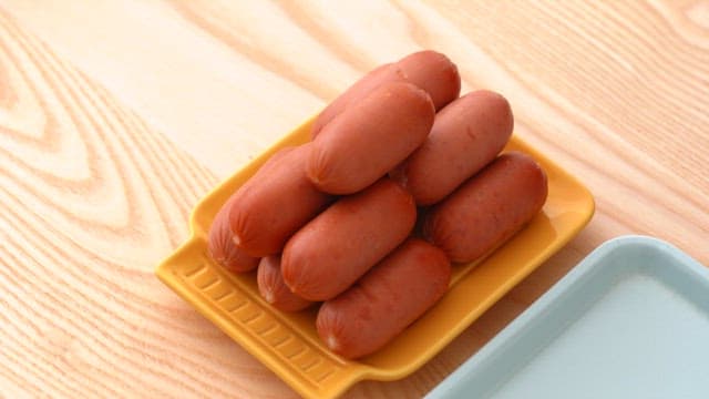 Arranged sausages on a yellow plate on a wooden table