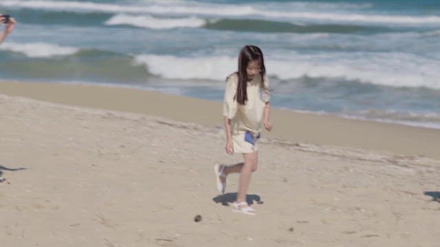 Young girl joyfully playing on a sandy beach with waves
