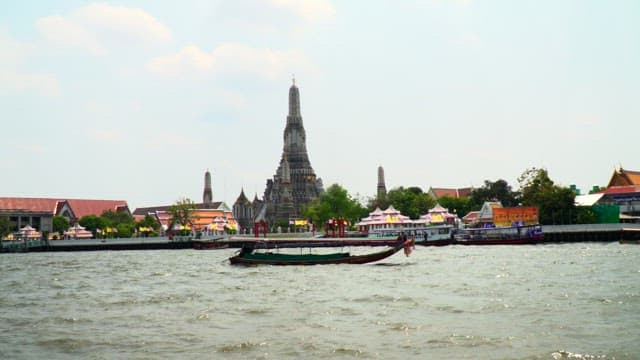 Boats crusing on the river with a temple visible in the distance at midday