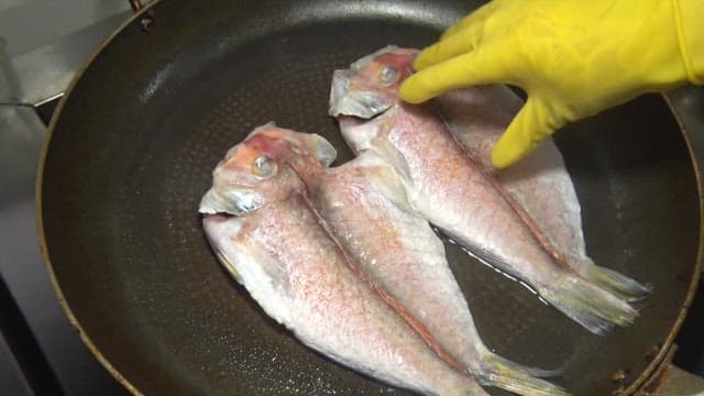 Grilling Fish in a Pan with a Yellow Glove