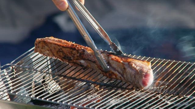 Grilling a large piece of meat on a barbecue grill with tongs outdoors