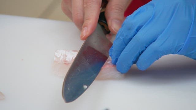 Slicing raw fish delicately with a knife on a cutting board