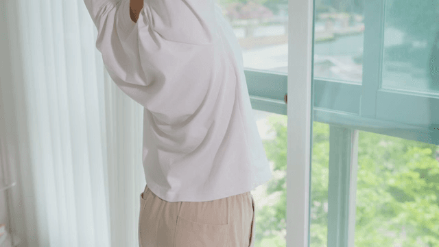 Person Stretching by a Window Overlooking Greenery