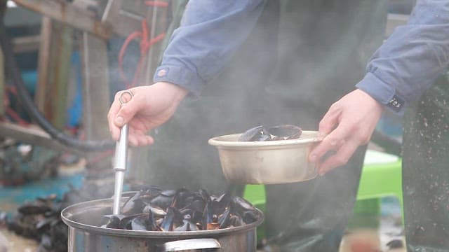 Person ladling fresh mussels cooking in a pot
