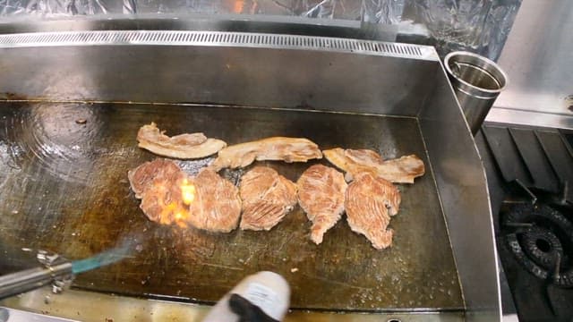 Grilling Meat with Flames of Torch on a Flat Grill