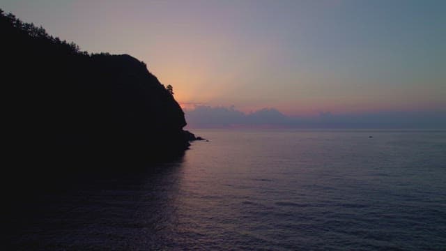 Sunset over a calm ocean and cliff
