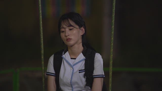 Contemplative student wearing a school uniform sitting on a swing at night