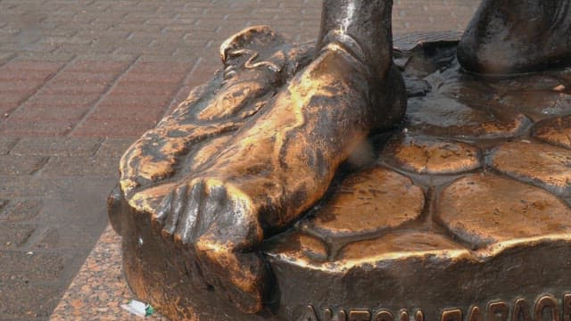 Wet bronze statue foot on stone pavement