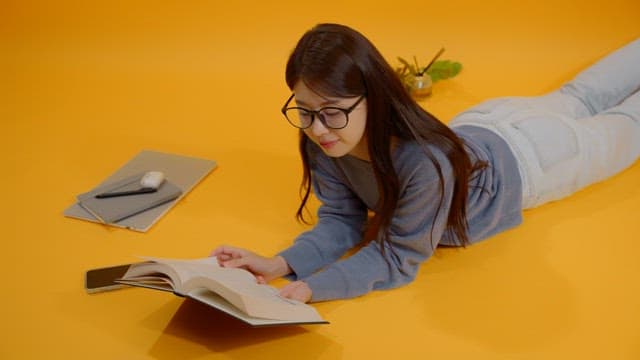 Woman reading a book while lying on her stomach in a bright room