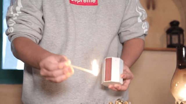 A person lighting an oil lamp with a matchstick indoors.