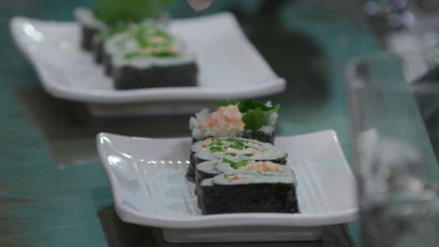 Sesame seeds sprinkled over gimbap plated on a white plate