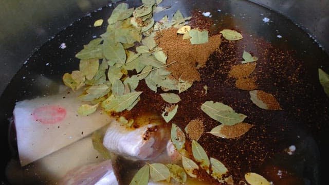 Chef adding bay leaves and spices to a cooking pot with meat