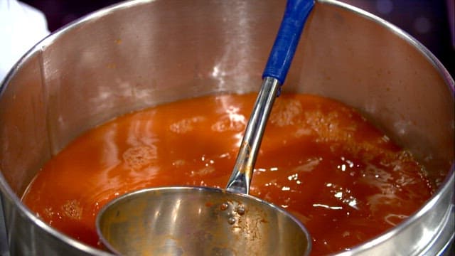 Stirring red broth with ladle in a large pot