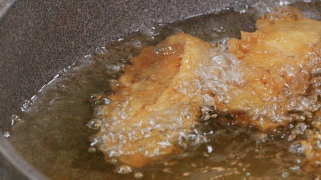 Four pieces of battered fish frying in hot oil in a pan