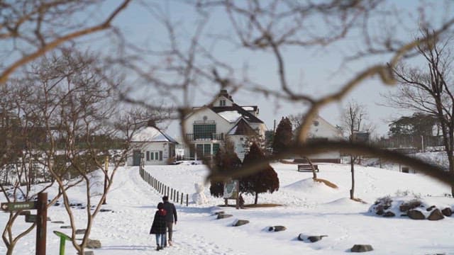 Couple Walking on Snowy Path by House