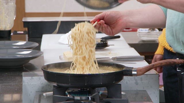 Adding pasta noodles into a frying pan with boiling sauce