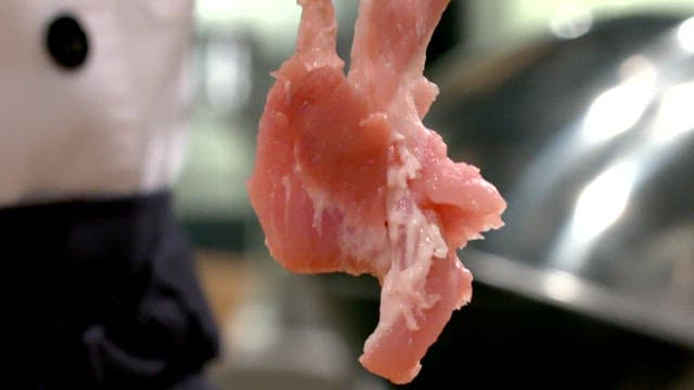Chef holding raw pork ribs being trimmed in the kitchen