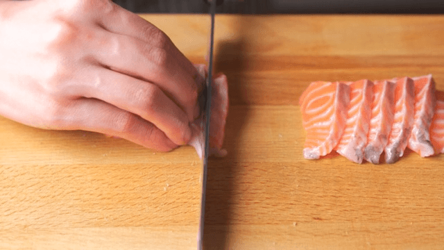 A person slicing fresh salmon on a wooden cutting board