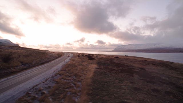 Car driving on a coastal road at sunset