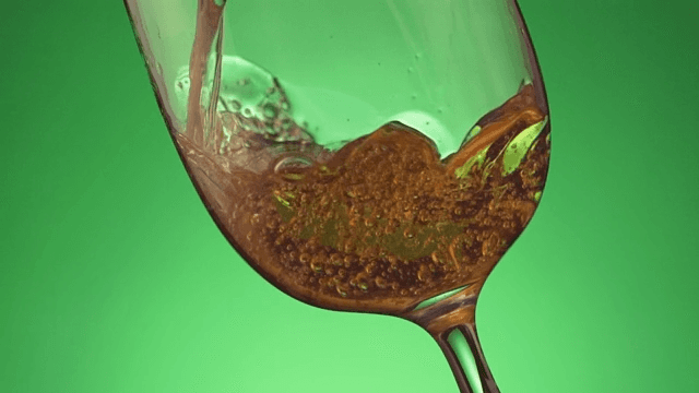 Pouring carbonated drinks into wine glass on green background