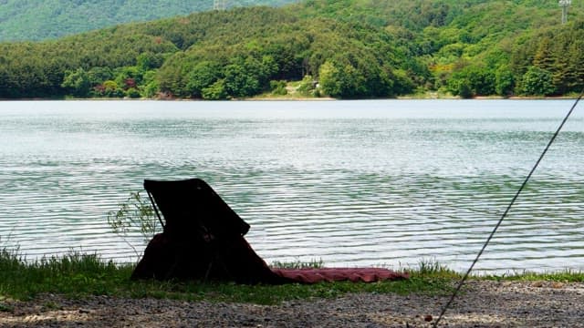 Man prepating camping gear on a chair by a lakeside with lush green forest in the background