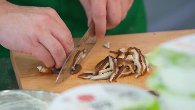 Person slicing mushrooms on a wooden cutting board with knife