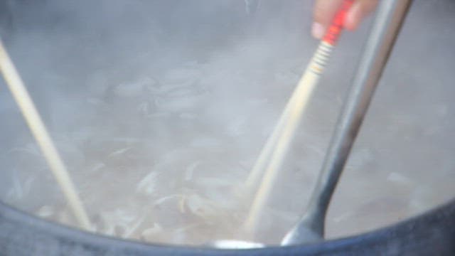 Noodles being stirred in a steaming pot with ladle