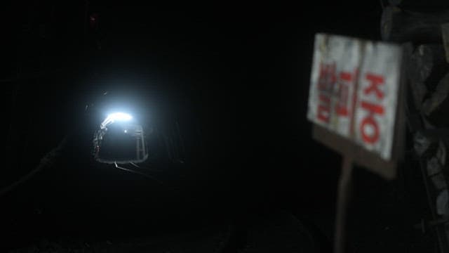 Industrial mine tunnel with a mining cart and 'blasting in progress' warning sign