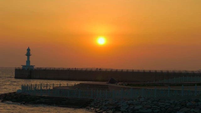 Sunset behind a white lighthouse by the sea