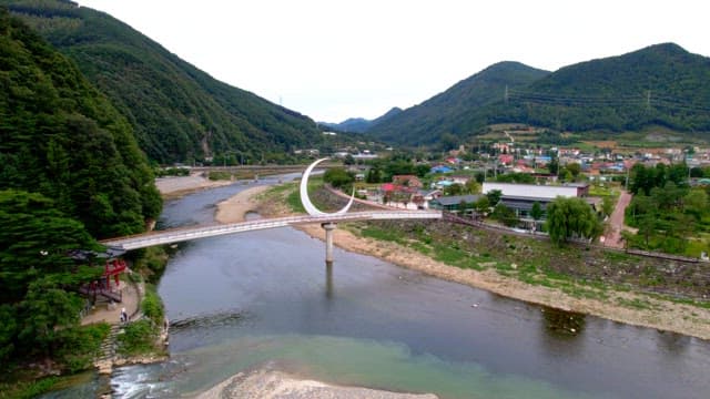 Scenic view of a serene countryside with a crescent-shaped bridge spanning over a peaceful river