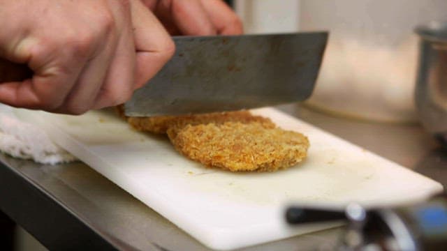 Slicing fried cutlets on a chopping board.