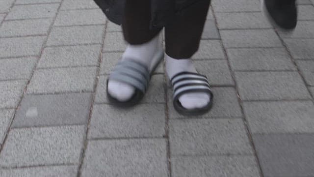 Feet walking on the sidewalk wearing black pants and slippers