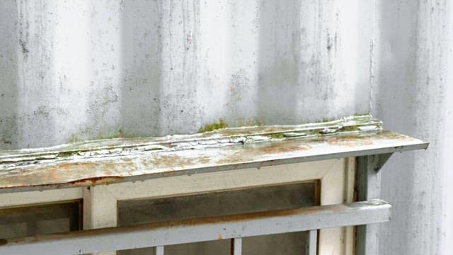 Raindrop falling on rusty windowsill with moss growth against a weathered wall of conatiner building