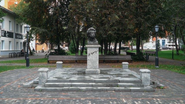 Bust statue of Pushkin in a park surrounded by trees on a cloudy day