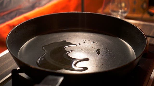 Raw meat being placed into a heated frying pan with oil