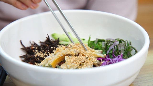 Mixing Korean bibimbap with fresh vegetables and abalone with chopsticks