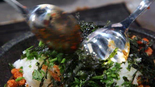 Stir frying bibimbap with fresh vegetables on a hot plate