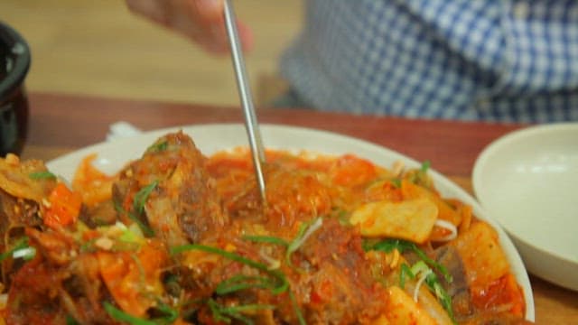 Chopsticks lifting glass noodles from spicy braised pork backbone