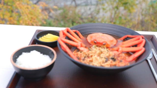 Bowl of warm ramen with red snow crab, rice, and a plate of pickled radish