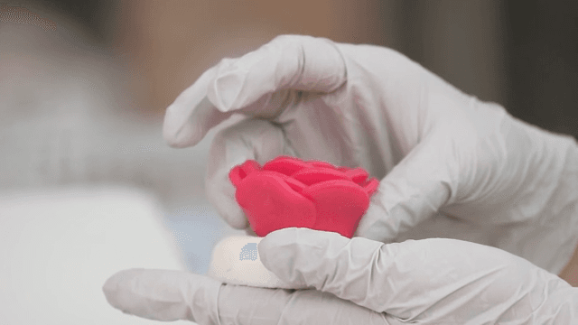 Gloved hands shaping icing into decorative flowers on a baking mat