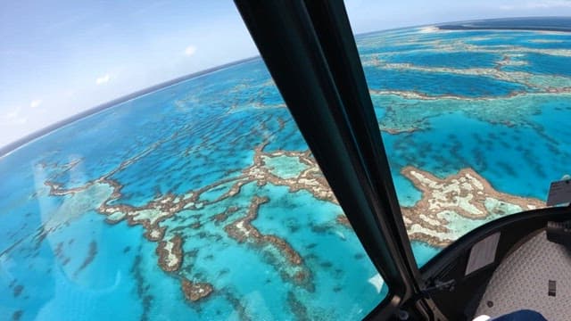 Emerald corals embroidered on the vast sea as seen from a helicopter