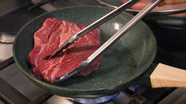 Beef steak being cooked in a frying pan